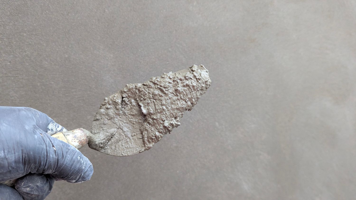 A trowel loaded with fresh plaster against a hand-finished wall — the stage that decides the finish